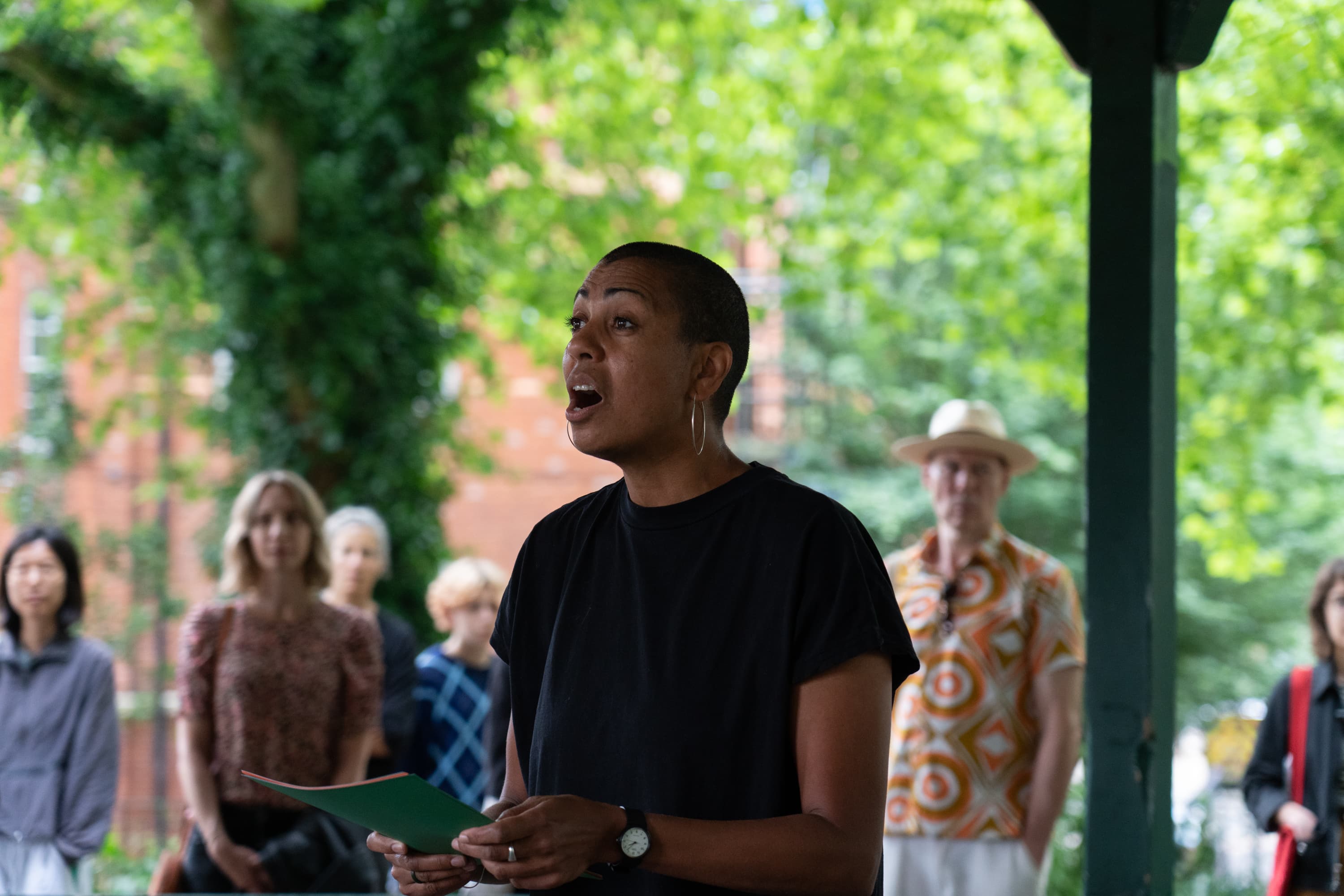 The artist Helen Cammock giving a reading of one of her perfomances. In the background is a poster that says I can hear your lament