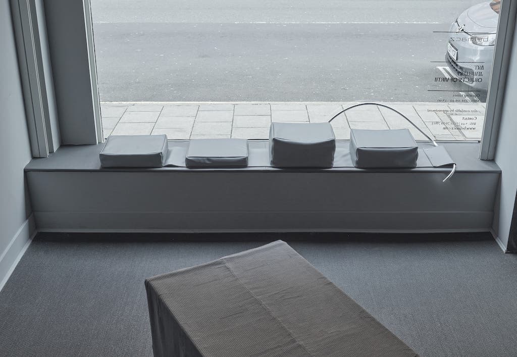 Installation shot of Seat for a boy by Agata Madejska consisting of a series of cushions and tubular steel sculpture on a ledge in front of a window