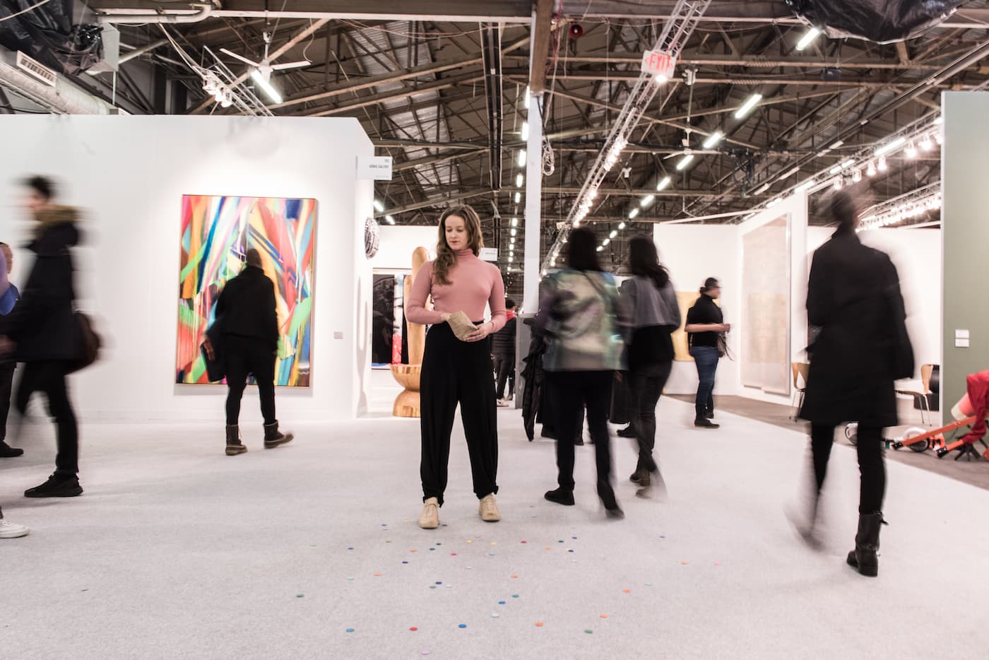 A female performer standing on the middle of an art fair throwing peices of circular confetti to the ground.