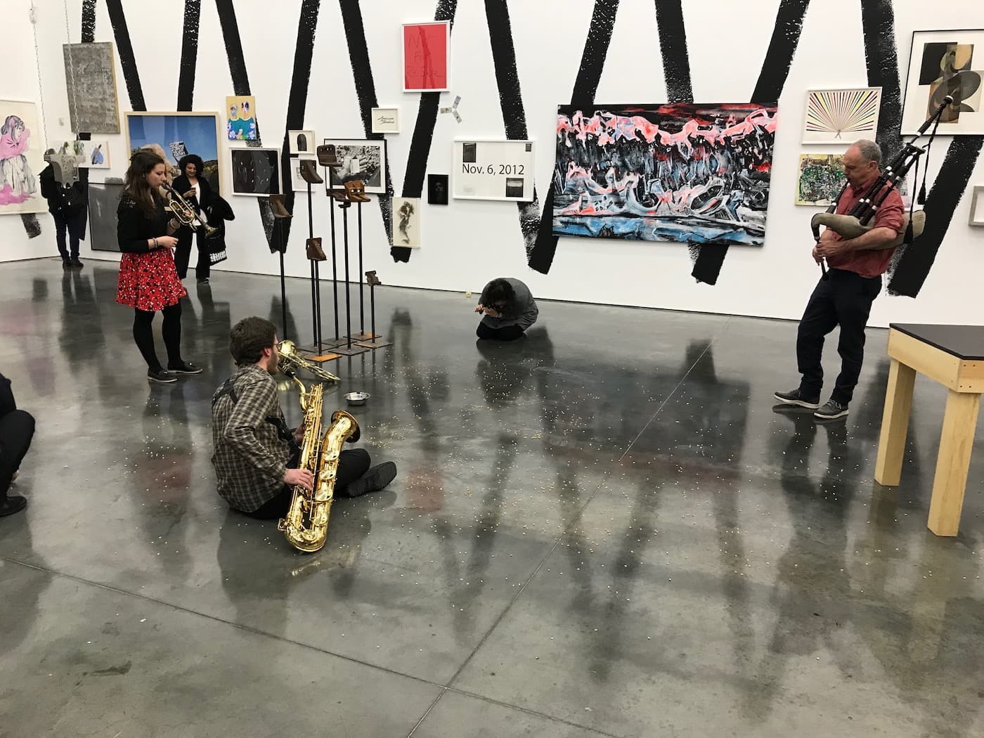 A group of musicans in a gallery, some sat on the floor, playing various instruments to un-popped popcorn kernals