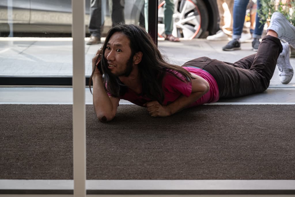 A performer crawling on their front through a door to a gallery while on the phone