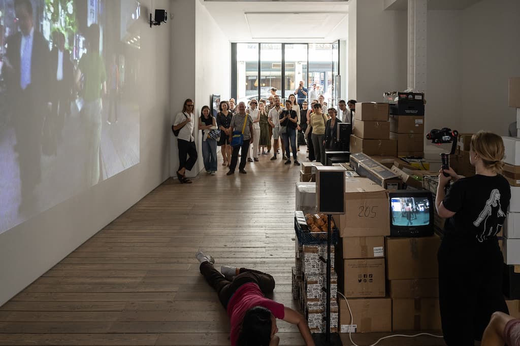 A performer crawling on their front in a gallery space while on the phone