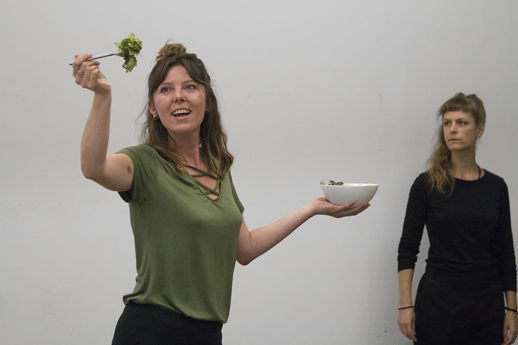 A woman holding a bowl of salad in one hand and a fork with lettuce in the other performing Woman with Salad by Emily Perry