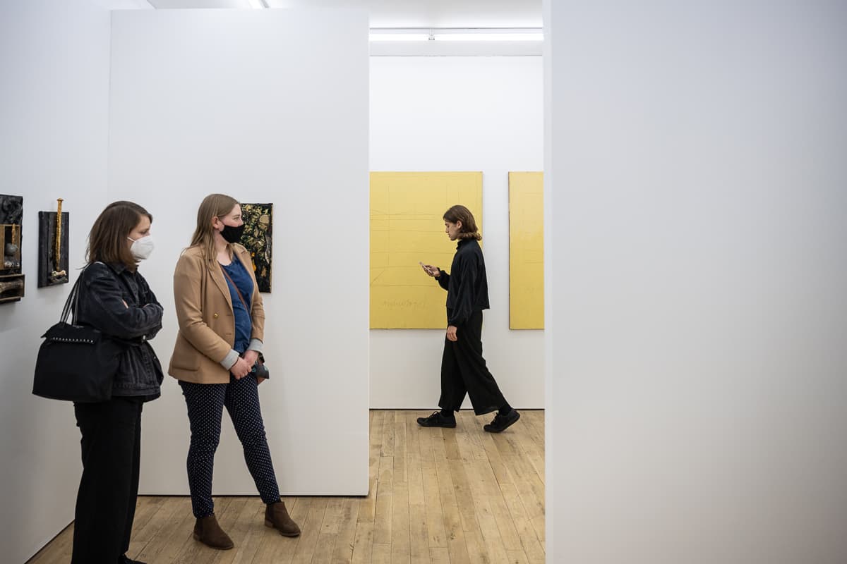 The artist Heman Chong standing in a gallery space reading from a smart phone - performing Everything (Wikipedia)