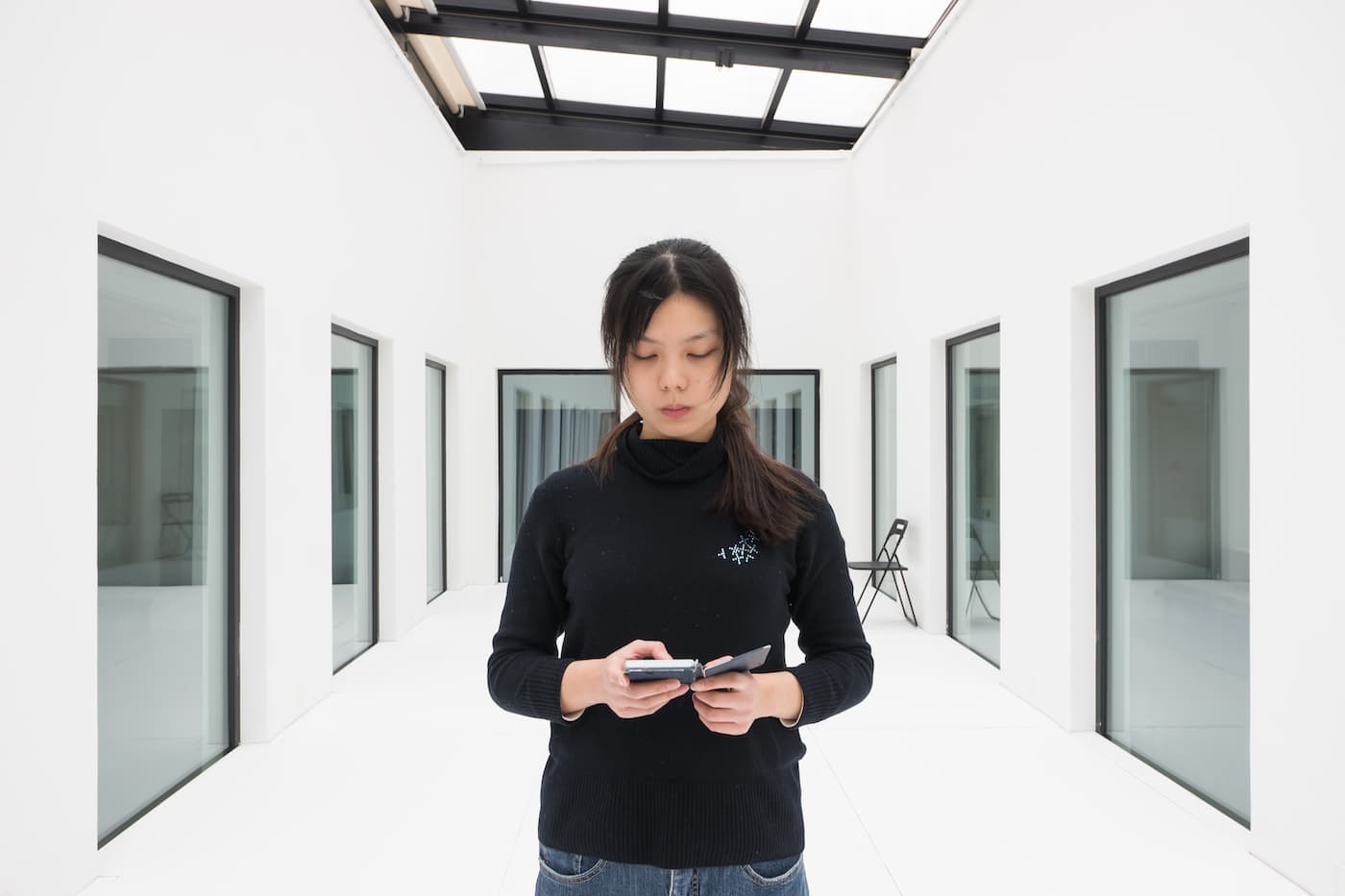 The artist Heman Chong standing in a gallery space reading from a smart phone - performing Everything (Wikipedia)
