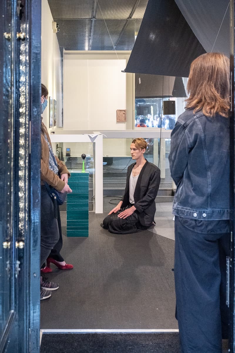 Still from performance of A Case of Med(ling)tation, with performer kneeling with arms spread wide.