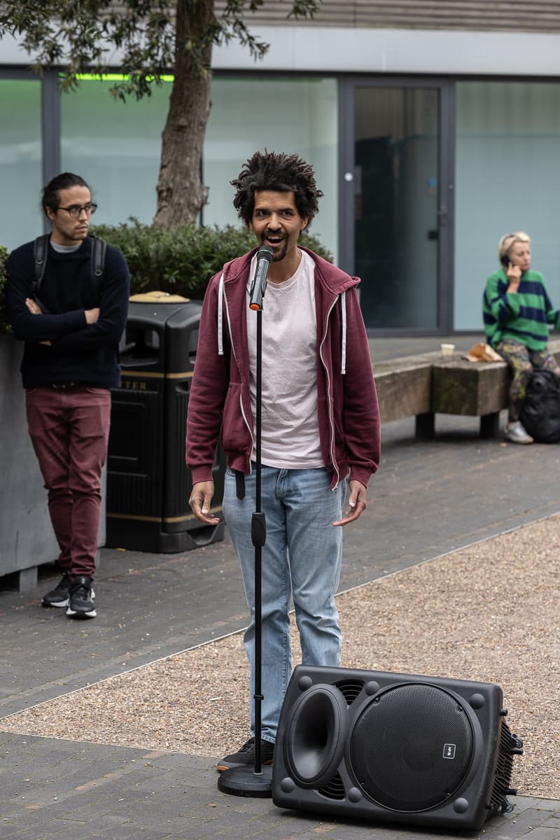 A performer with a microphone and a sub-woofer standing outside VITRINE Gallery.