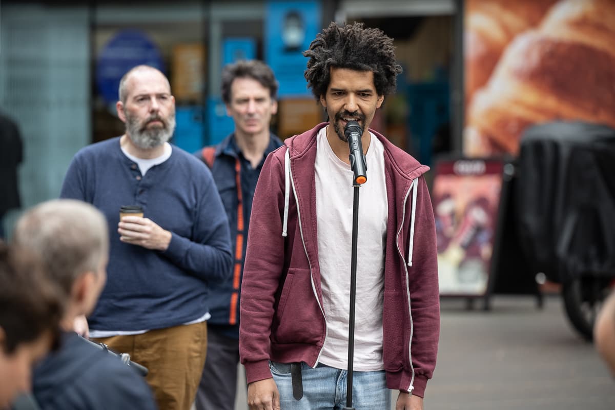 A performer with a microphone and a sub-woofer standing outside VITRINE Gallery.