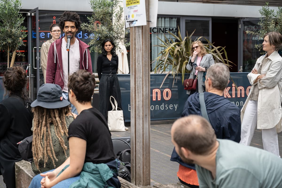 A performer with a microphone and a sub-woofer standing outside VITRINE Gallery.