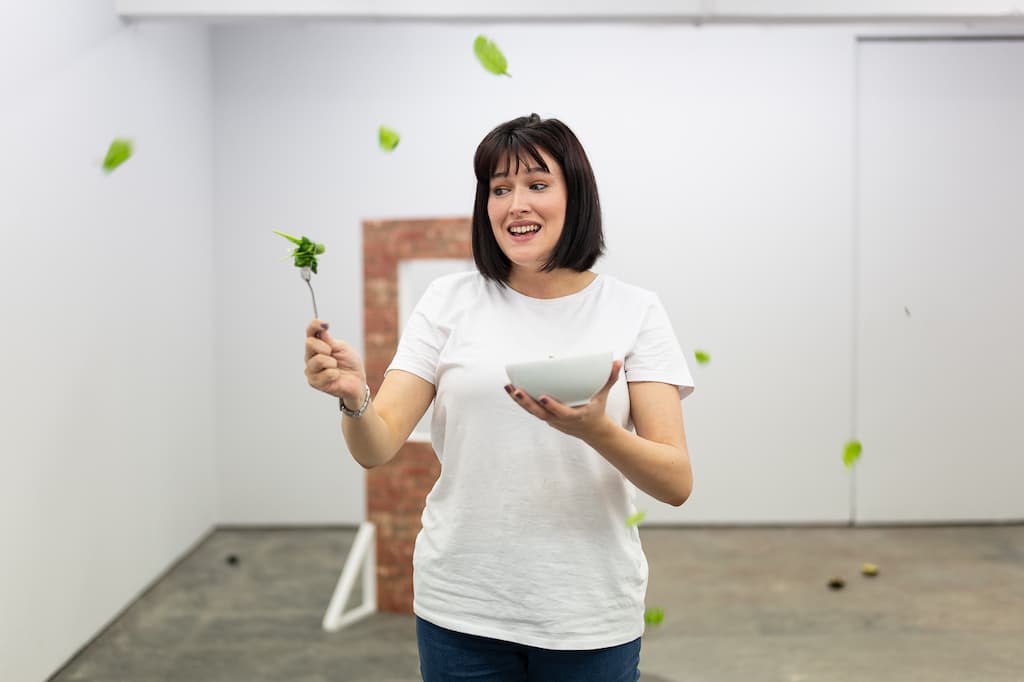 A performer holding a bowl of salad in one hand and a fork with lettuce in the other.