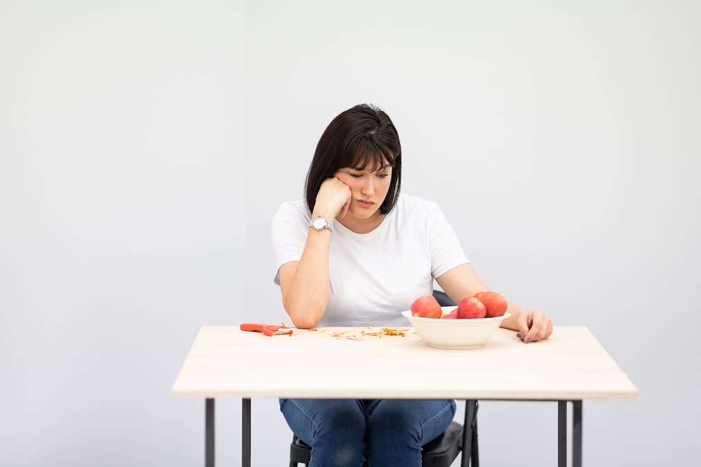 A performer sat at a table with a bowl of apples, looking bored.