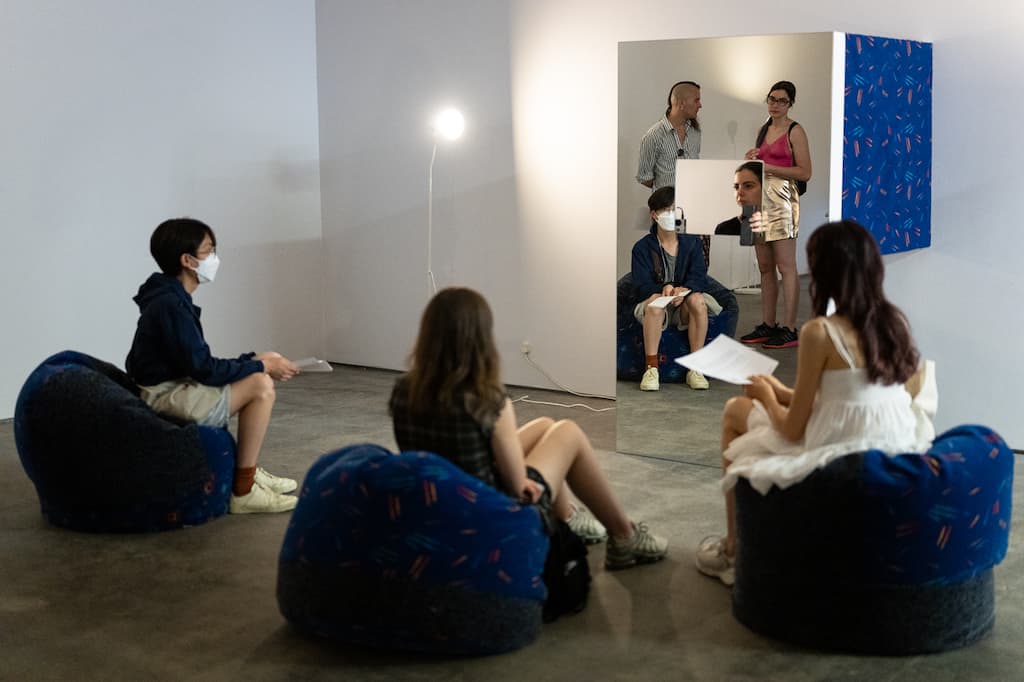 A performer sat in a mirrored booth, with audience in the foreground sat on beanbags.