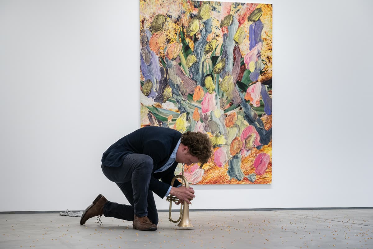 A group of musicans in a gallery, some sat on the floor, playing various instruments to un-popped popcorn kernals