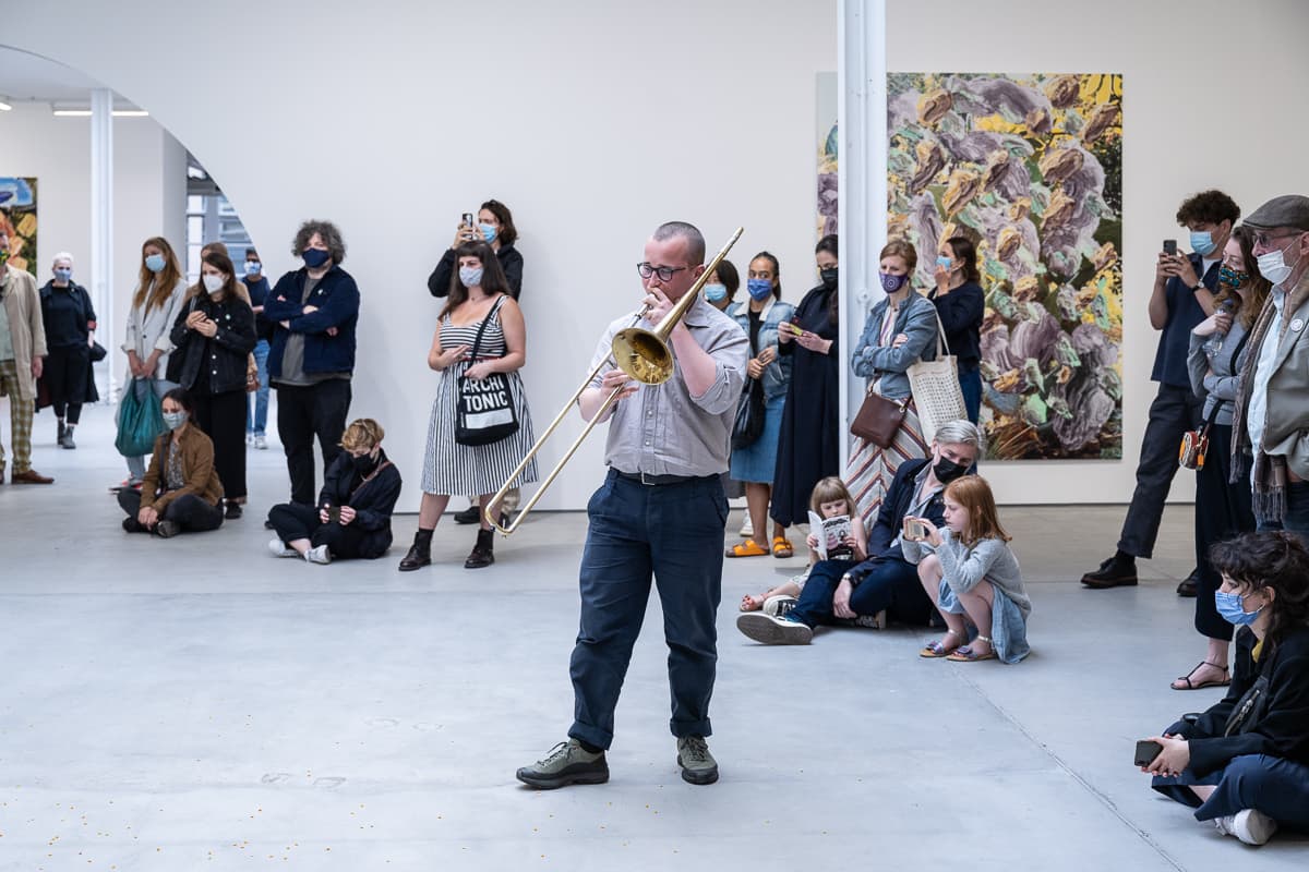 A group of musicans in a gallery, some sat on the floor, playing various instruments to un-popped popcorn kernals