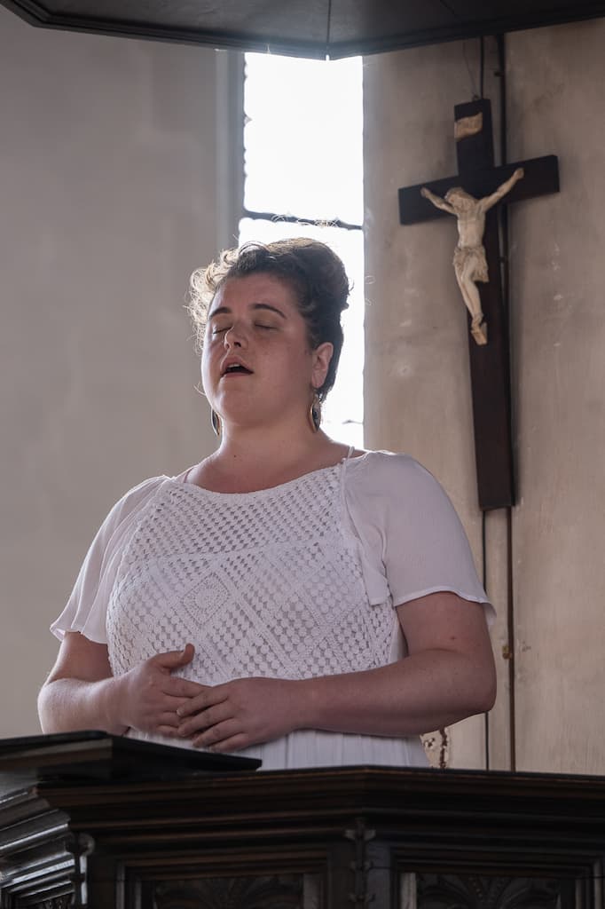 A performer singing at a woodern lecturn with a crucifx in the background