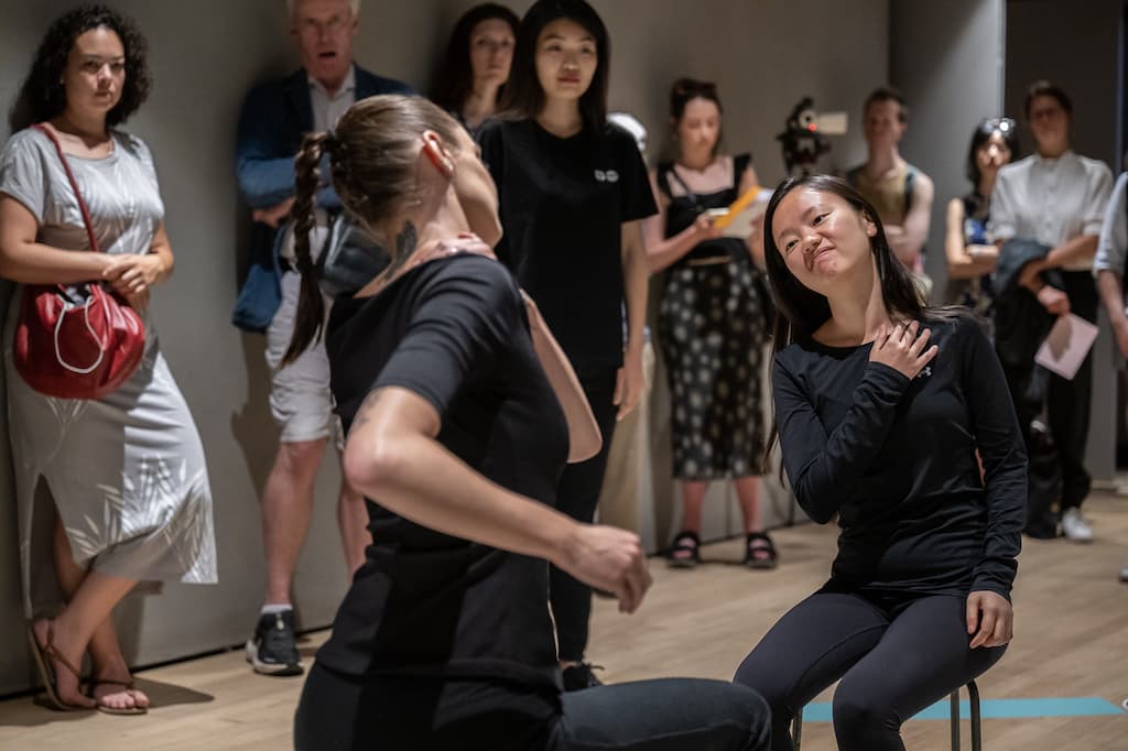 Installation shot showing two performers sat in the middle of the pentagram with their arms on their shoulder, leaning to one side and mirroring each others pose.