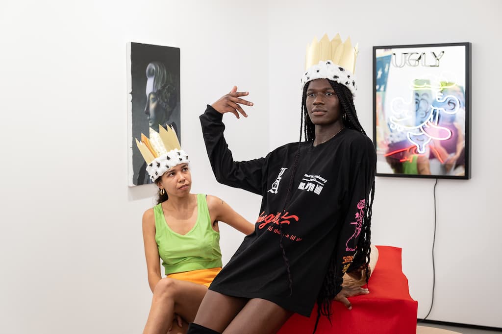 Two performers, both wearing crown. One is sitting on a chair, the other on a table.